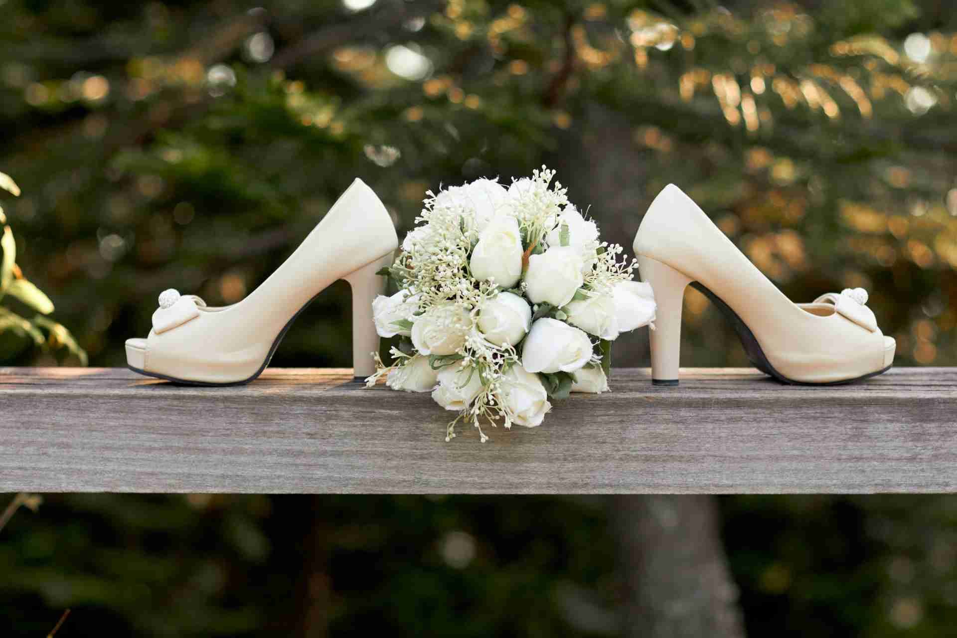 Pair of beige high heels with a white rose bouquet placed between them on a wooden rail