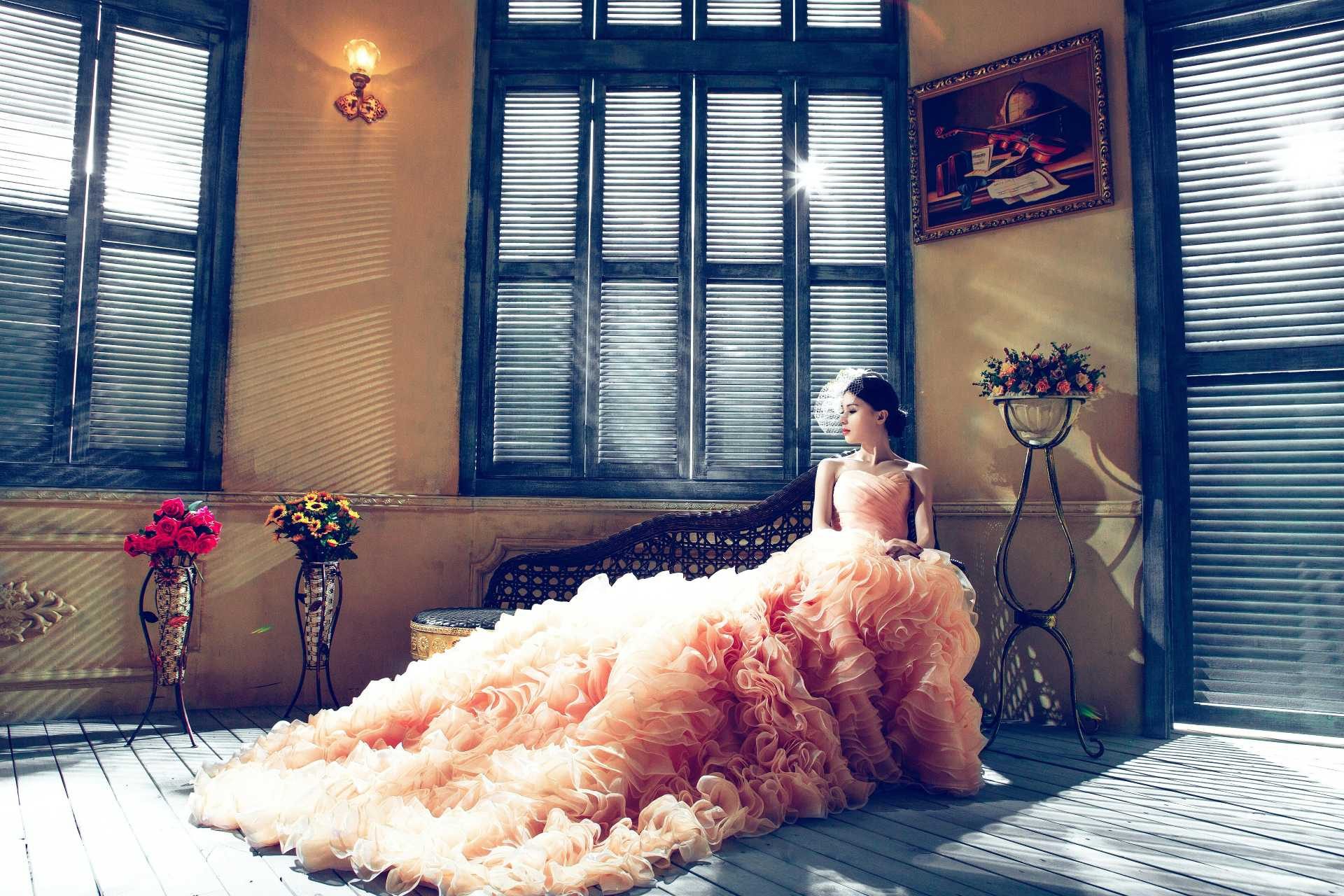 Woman in a peach ruffled gown sitting on a vintage couch in a softly lit room
