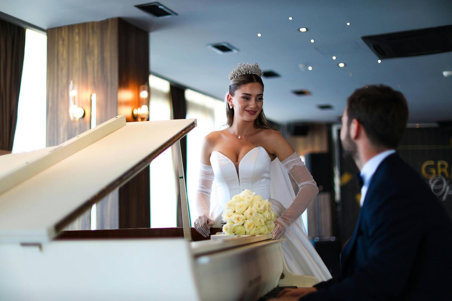 Bride in a white gown holding a bouquet of roses while standing next to a pianist