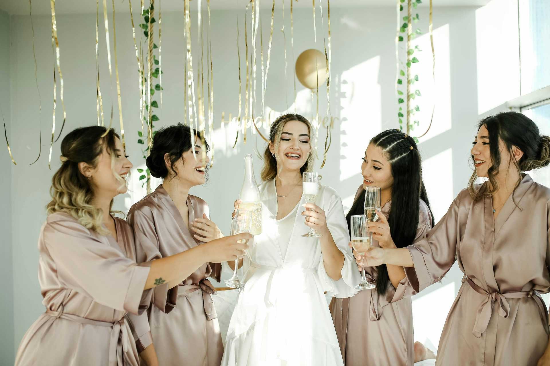 Bride and bridesmaids in satin robes celebrating with champagne