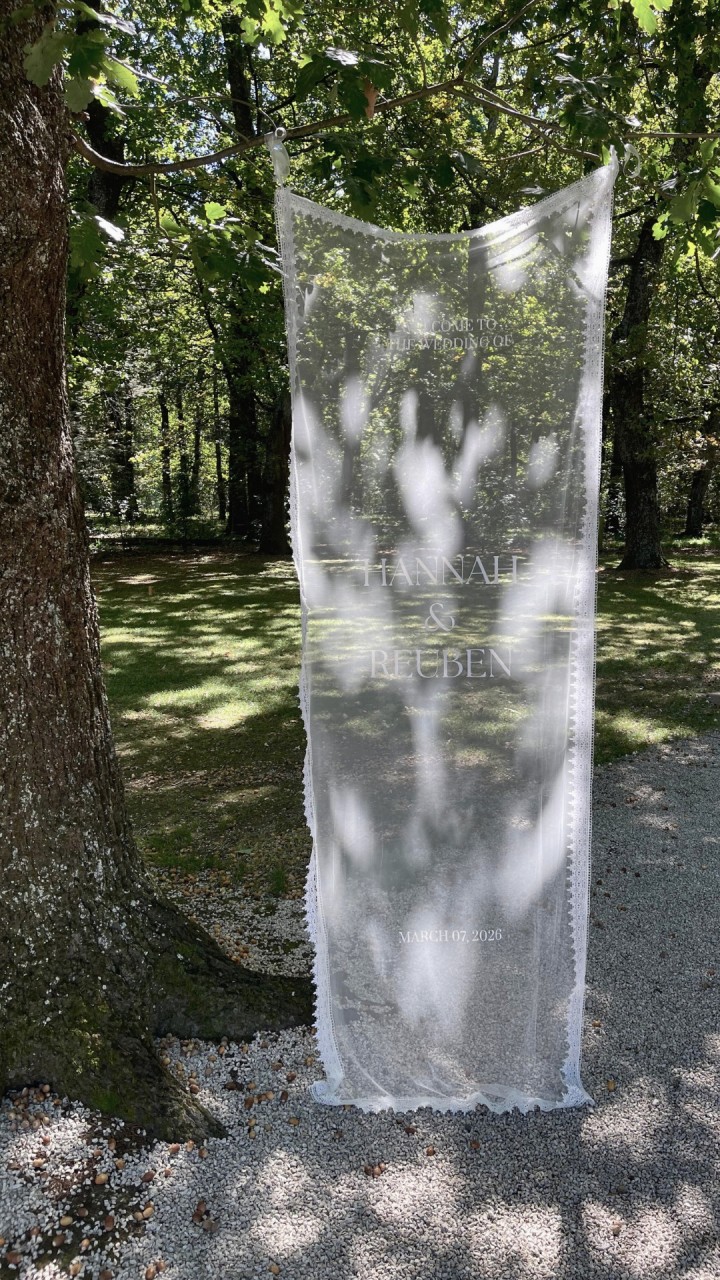 DIY Lace Wedding Welcome Sign

Create a soft, romantic welcome for your guests with this beautiful lace wedding sign, a simple DIY that adds a personal touch to your special day.

What you'll need:
• Tulle fabric (amount depends on how large you'd like your sign)
• Cricut machine
• Cricut Smart Iron-On Vinyl (white)
• Iron
• Needle and thread
• Lace trim
• Baking paper

How to make it:

1.) Cut your base
Cut the tulle fabric to your desired sign size.

2.) Create the lace border
Lay the lace trim around the edges of the tulle and cut it to fit, forming a delicate border.

3.) Design your text
Head to Canva and experiment with fonts until you find one that feels perfect for you and your partner.

4.) Prepare your Cricut design
Import your design into Cricut Design Space and remember to mirror the design before cutting so it transfers correctly when ironed.

5.) Weed the vinyl
Remove the excess vinyl around your lettering.

6.) Position your design
Place the vinyl where you'd like the wording to appear on the tulle.

7.) Iron it on
Make sure your iron is set to dry heat (no steam). Place baking paper on top of the vinyl and underneath the tulle to protect the fabric.
Apply the iron gently,  tulle is delicate, so this step may take a few passes. Be patient and use a low heat setting.

8.) Remove the carrier sheet
Slowly peel away the plastic layer. If the vinyl lifts, simply reapply heat until it adheres properly.

9.) Attach the lace
Hand-stitch the lace trim around the edge of the tulle for the best finish. (A hot glue gun or iron-on lace can work if you're short on time.)

And just like that, you have a romantic lace welcome sign ready to greet your guests. A beautiful handmade detail for your wedding day 🤍